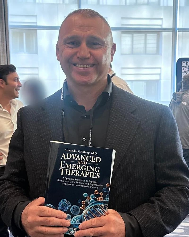 Alexander Grinberg, M.D., holding an advance reader copy of Advanced and Emerging Therapies at the Abundance Longevity Trip 2026